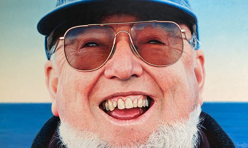 Oil painting by Josonia Palaitis depicting a close up view of the face of Thomas Keneally smiling with his teeth showing wearing sunglasses and a blue cap with the ocean horizon in the background