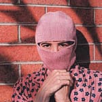 Self portrait painting by Josonia Palaitis depicting the artist wearing a pink balaclava and standing in front of a brick wall