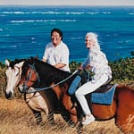 An oil painting by Josonia Palaitis depicting a couple on horseback in fron to a big blue ocean