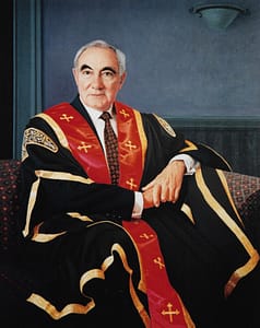 Oil painting by Josonia Palaitis depicting Professor Peter Drake sitting on a couch in a formal pose wearing his ceremonial robes in black, gold and red