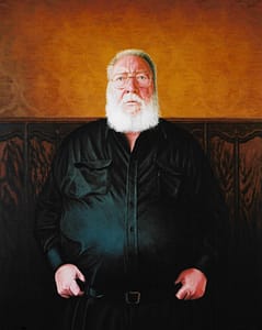 Oil on canvas portrait painting by Josonia Palaitis depicting journalist Paddy McGuiness standing and wearing a black shirt with his thumbs tucked into his belt wearing his glasses and sporting a big white beard