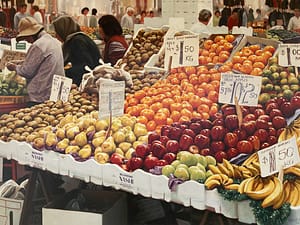 Oil Painting by Josonia Palaitis depicting a colourful fruit stall with apples, bananas, pears and mandarins with people browsing in the background